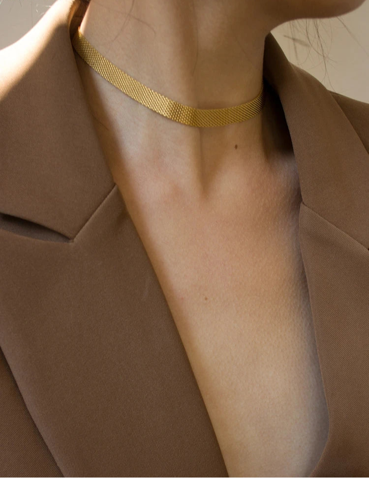 Goldene, flache Schlangenkette aus Titan an Frau getragen | Schimmernder, kurzer Halsschmuck zum Blazer | Gold-Kette elegant