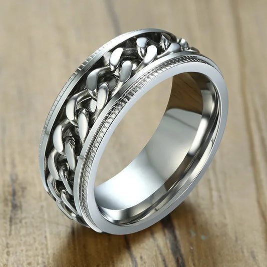 Detailaufnahme eines glänzenden Edelstahl-Drehrings für Herren mit geschwärzten Akzenten im Ketten-Design auf einer Holzoberfläche.