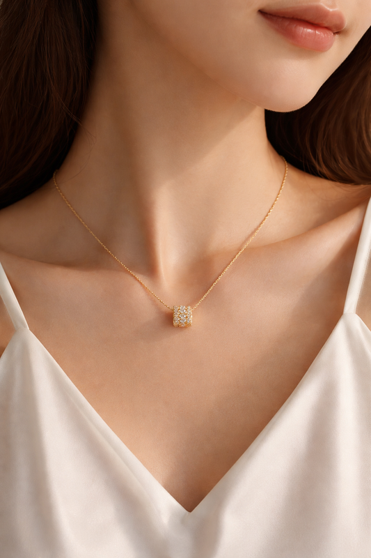 Eine Frau trägt die filigrane, goldvergoldete Edelstahlkette mit dem zylindrischen Zirkonia-Anhänger zu einem weißen Top, um die Proportionen und den Glanz am Dekolleté zu zeigen.