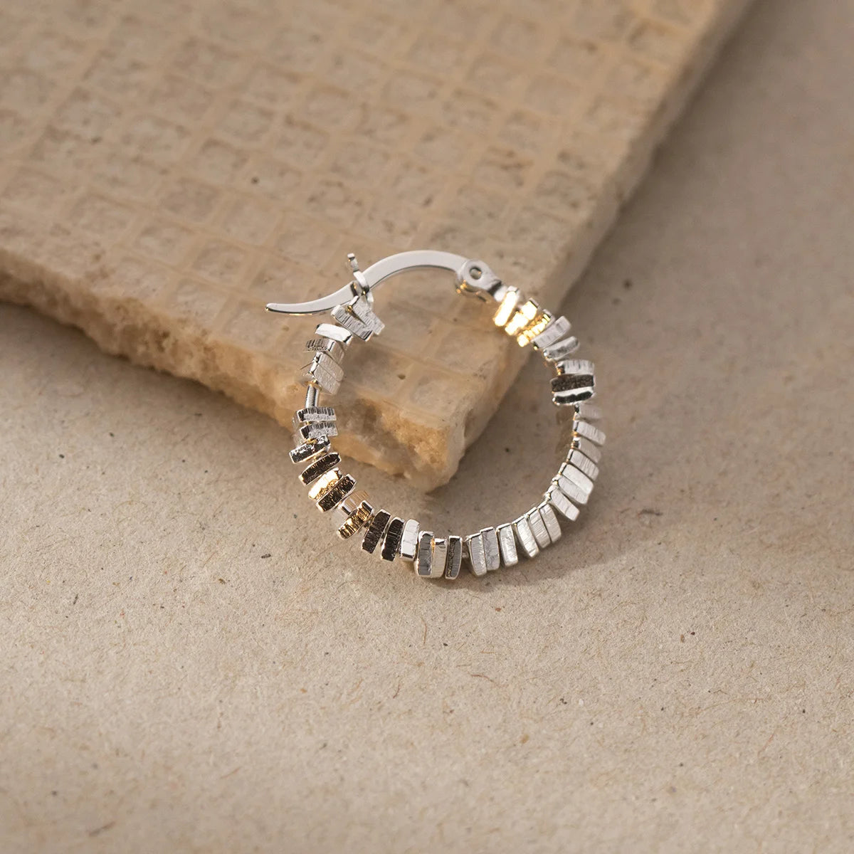 Ein einzelner Kreolen-Ohrring (925er Silber) mit auffälliger Rillenstruktur liegt seitlich auf einer hellbraunen Oberfläche.