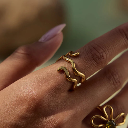 Detaillierte Nahaufnahme des gewellten, vergoldeten Edelstahlrings am Zeigefinger einer Frau, um das moderne Design und die Passform zu zeigen.