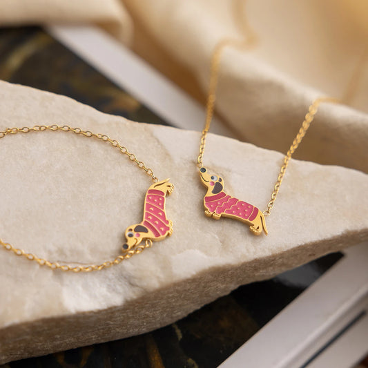 Nahaufnahme der Dackel-Halskette und des passenden Armbands aus vergoldetem Edelstahl, präsentiert auf einem hellen Naturstein.