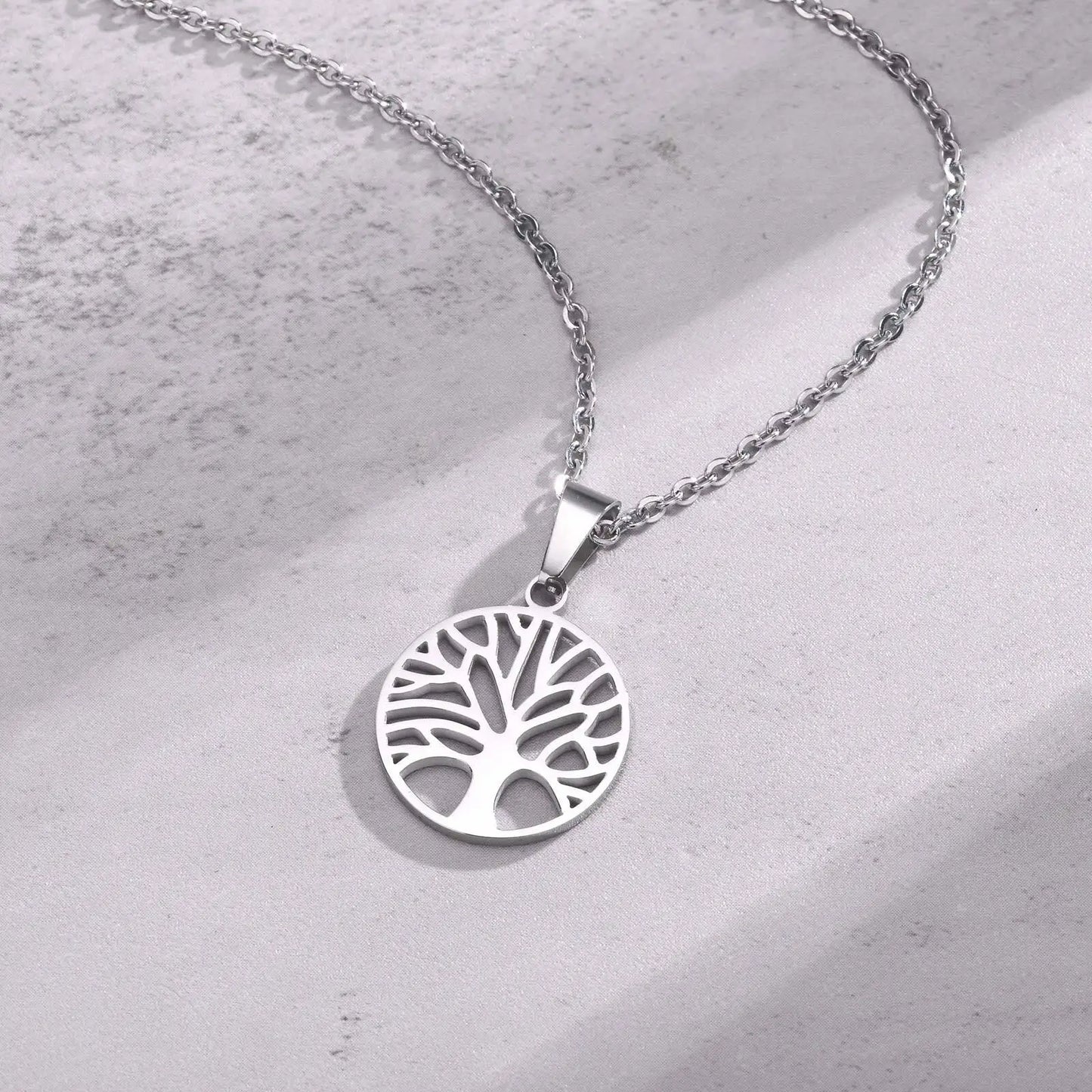 Detaillierte Studioaufnahme der silberfarbenen Edelstahlkette mit Lebensbaum-Medaillon, liegend auf hellem, strukturiertem Hintergrund.