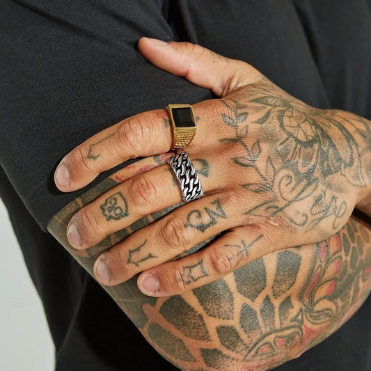 Sehr enge Nahaufnahme einer tätowierten Hand, die den breiten Edelstahl-Panzerketten-Ring trägt.