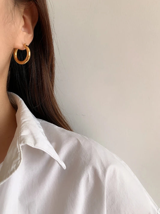 Minimalistische 18K vergoldete Creolen an einem Ohr einer Frau, die ein weißes Hemd trägt.