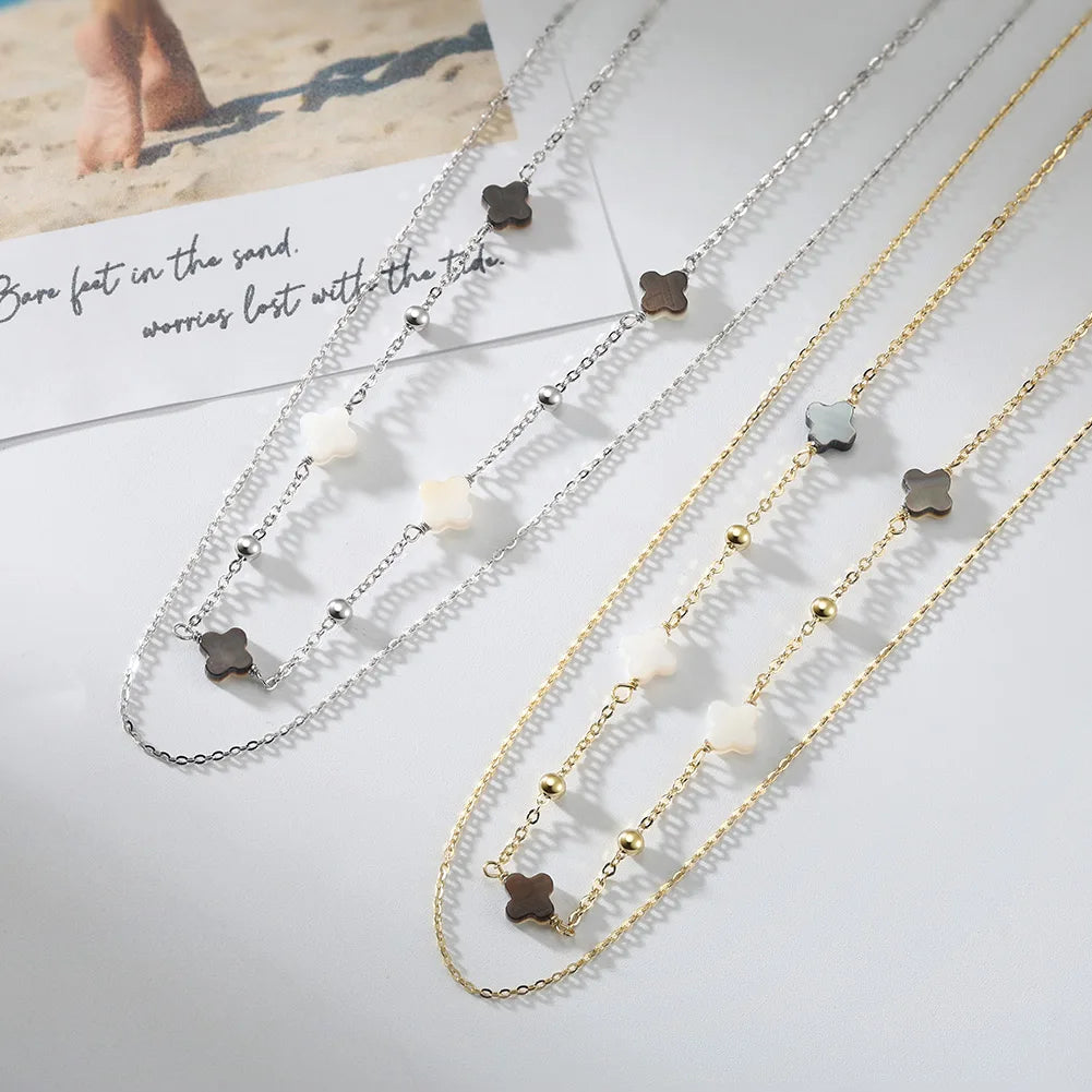 Mehrere goldene Halsketten mit beigen und schwarzen vierblättrigen Kleeblättern.