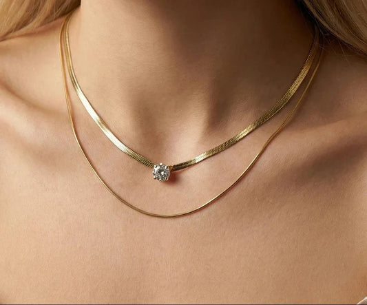 Eine Frau trägt eine zweireihige, vergoldete Edelstahl-Schlangenkette mit einem funkeldem Zirkonia-Stein.