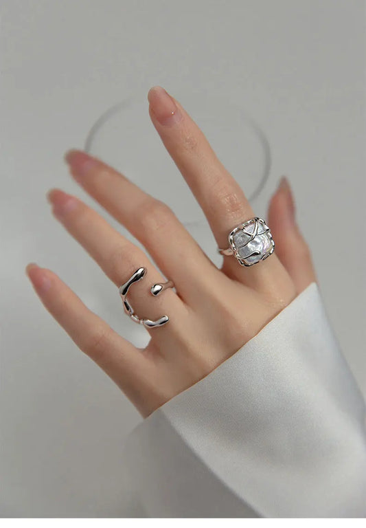 Hand einer Frau mit langen Nägeln, die einen großen, offenen 925er Silberring im Wickel-Design mit einem unregelmäßigen, facettenreichen Stein-Element trägt.