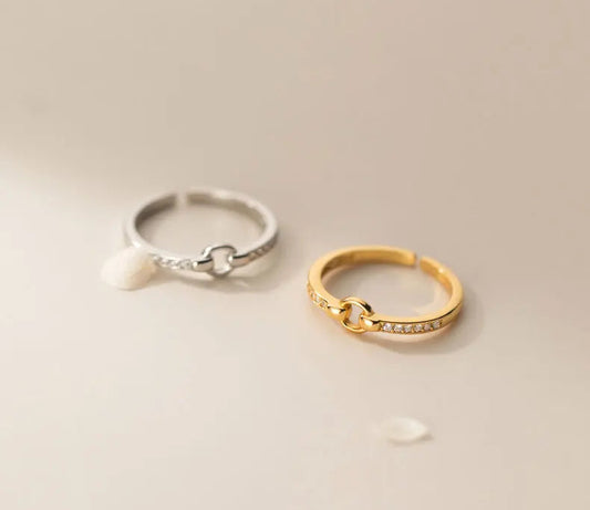 Minimalistisches Produktfoto: Der verstellbare Knoten-Ring in Silber und Gold nebeneinander auf einem beigefarbenen Hintergrund.