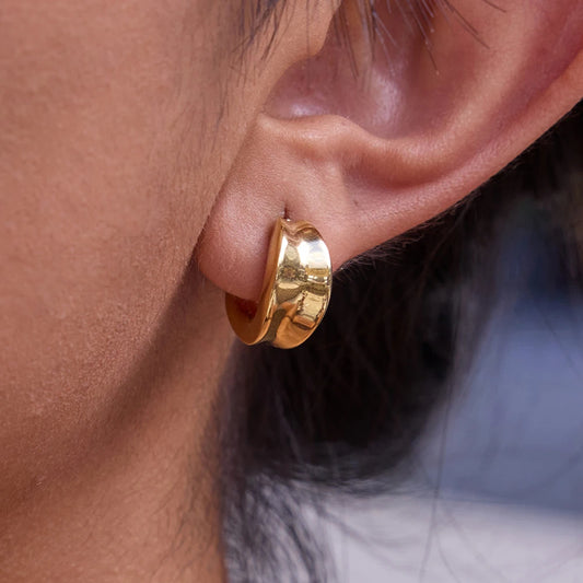 Eine Nahaufnahme des goldvergoldeten Edelstahl-Creolen-Ohrrings, um die Passform und Größe am Ohrläppchen der Trägerin zu demonstrieren.