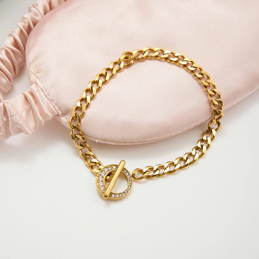 Das goldene Armband ist dekorativ neben einer rosa Schlafmaske aus Seide arrangiert, um die glänzende Oberfläche und das luxuriöse Design hervorzuheben.