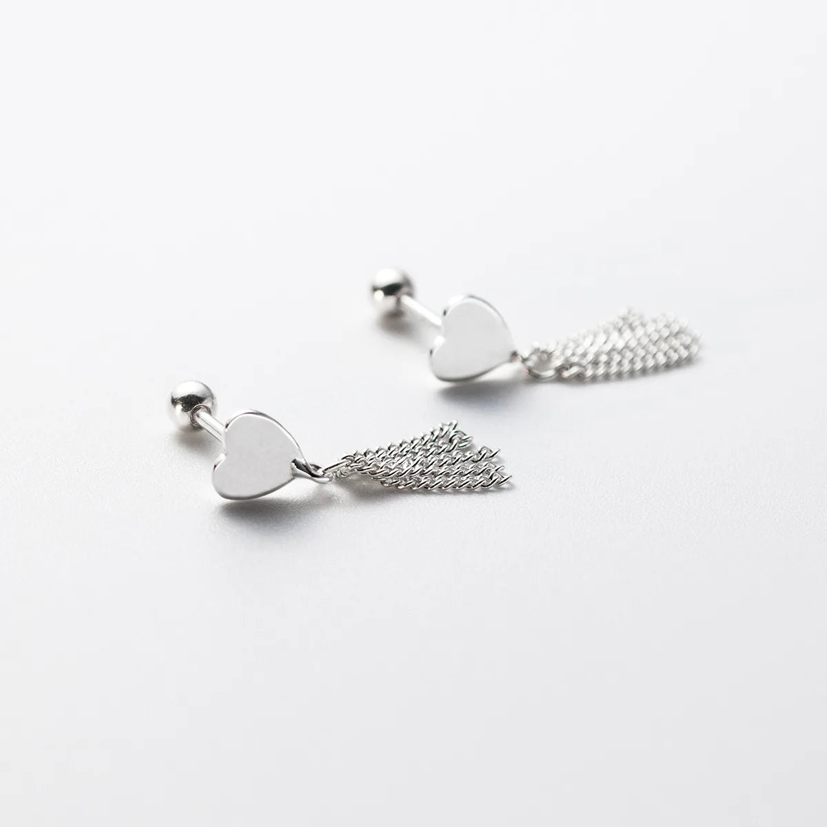 Ohrringe aus 925er Sterling Silber mit Herz-Motiv und feinen Fransen, flach liegend auf weißem Grund. Sichtbar ist der praktische Kugel-Schraubverschluss auf der Rückseite.