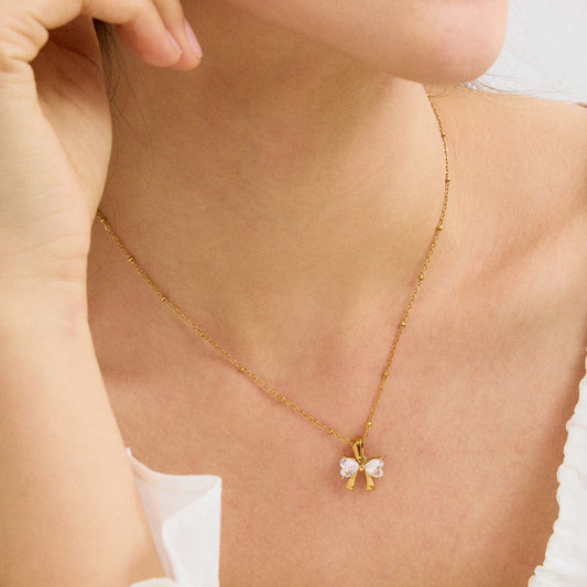 Model mit weißem Oberteil trägt eine zarte goldene Kette mit funkelndem Schleifenanhänger am Dekolleté