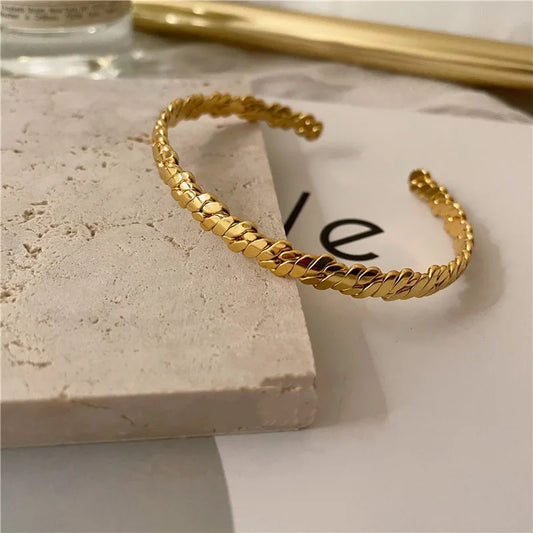 Offener Damen-Armreif aus Messing mit 18 Karat Gold-Vergoldung, 5,8 cm Innendurchmesser und geflochtener Textur auf Naturstein und Papier