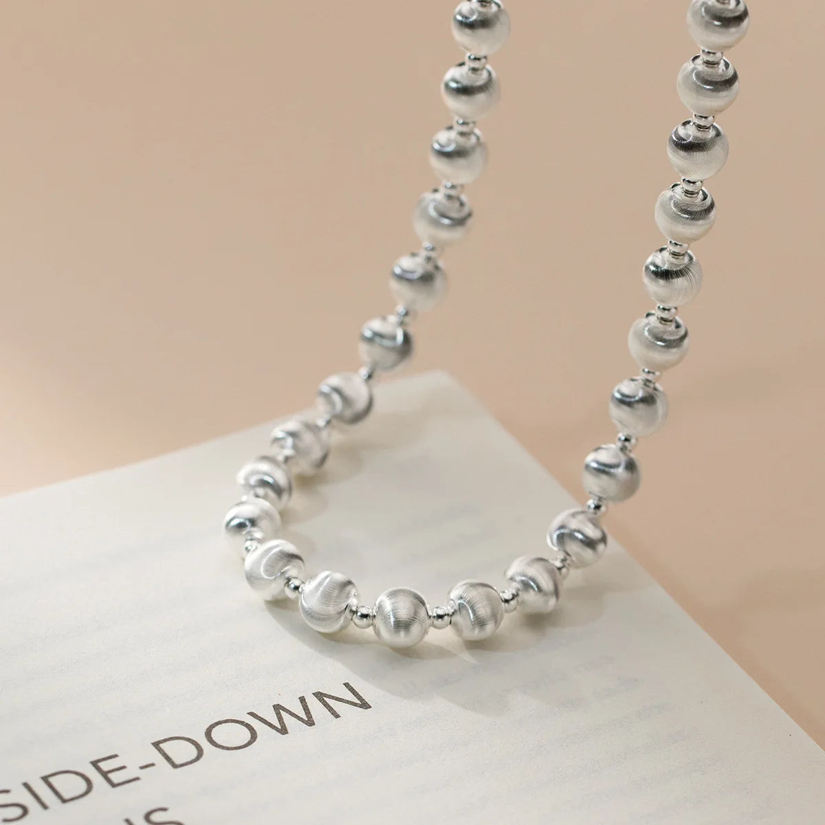 Kugelperlen-Halskette aus 925er Sterling Silber (mattiert und glänzend), die spiralförmig auf einem Buch liegt und den verstellbaren Verschluss zeigt.