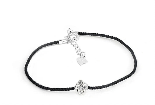 Nahaufnahme eines Armbands mit schwarzem Textilband und einem kleinen, runden Anhänger aus 925er Silber mit einem zentralen Zirkoniastein. Der Verschluss hat einen Herz-Anhänger aus 925er Silber.