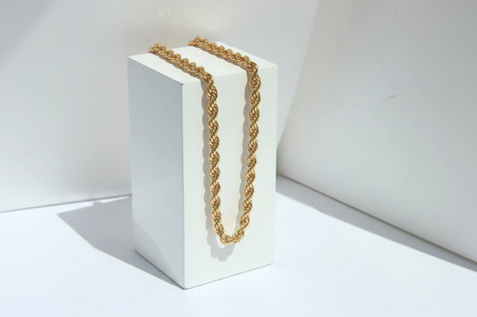 Nahaufnahme einer klobigen, gedrehten Goldkette drapiert auf einem weißen geometrischen Würfel.