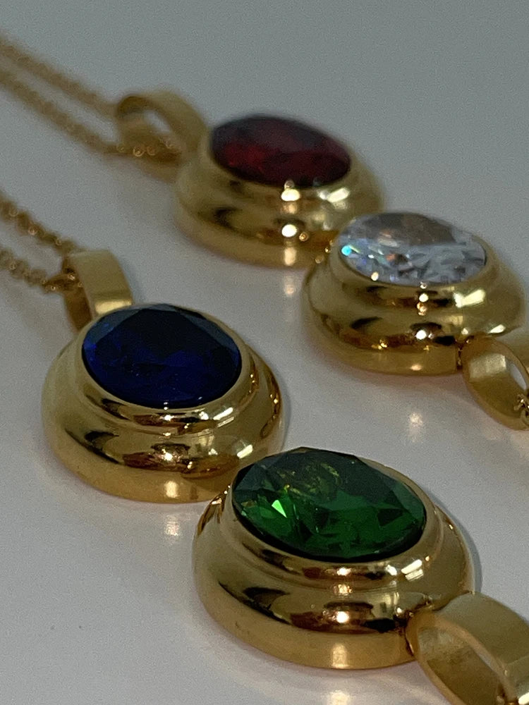 Detaillierte Nahaufnahme der ovalen, vergoldeten Titan-Anhänger mit eingefassten bunten Rhinestone-Steinen.
