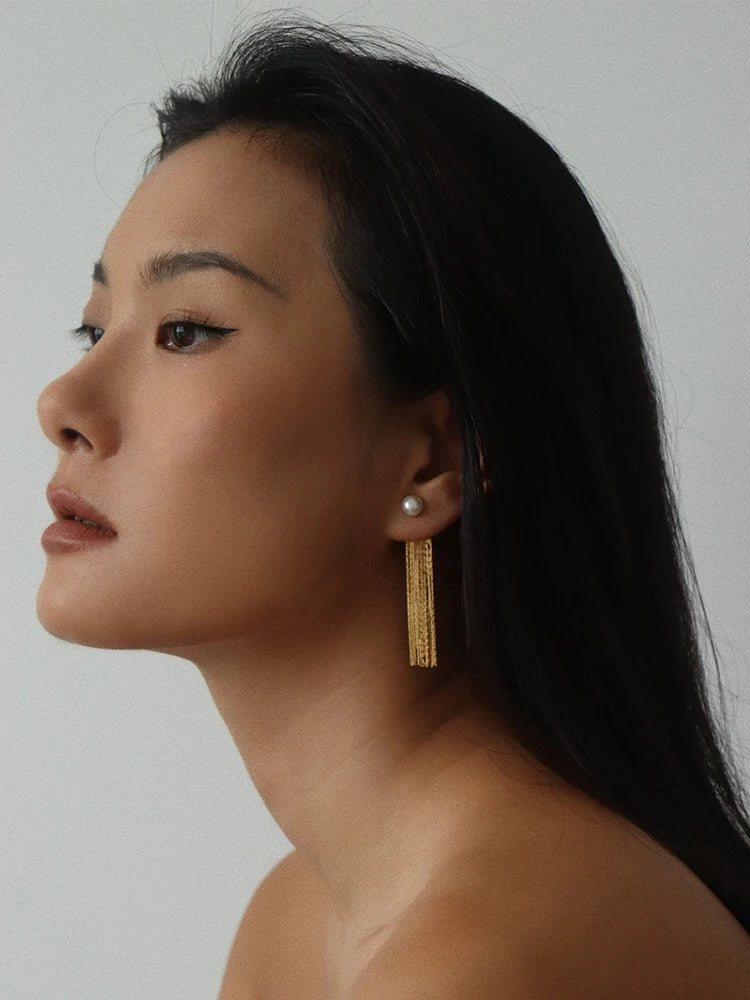 Seitenprofil einer Frau, das zeigt, wie die langen, goldfarbenen Fransenohrringe fließend fallen und einen luxuriösen Akzent zu einem minimalistischen Look setzen.