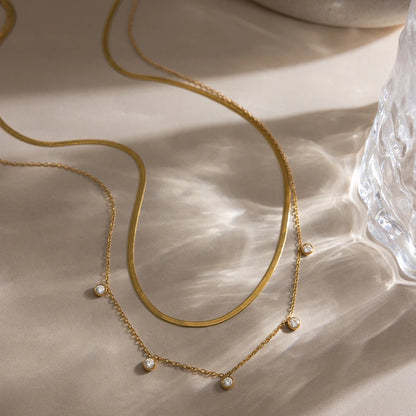 Nahaufnahme des geschichteten Gliederkettensets aus 18K goldvergoldetem Edelstahl, kunstvoll arrangiert in einer hellen, mattierten Steingutschale, um die Textur und den Glanz der Paperclip-Kettenglieder zu zeigen.