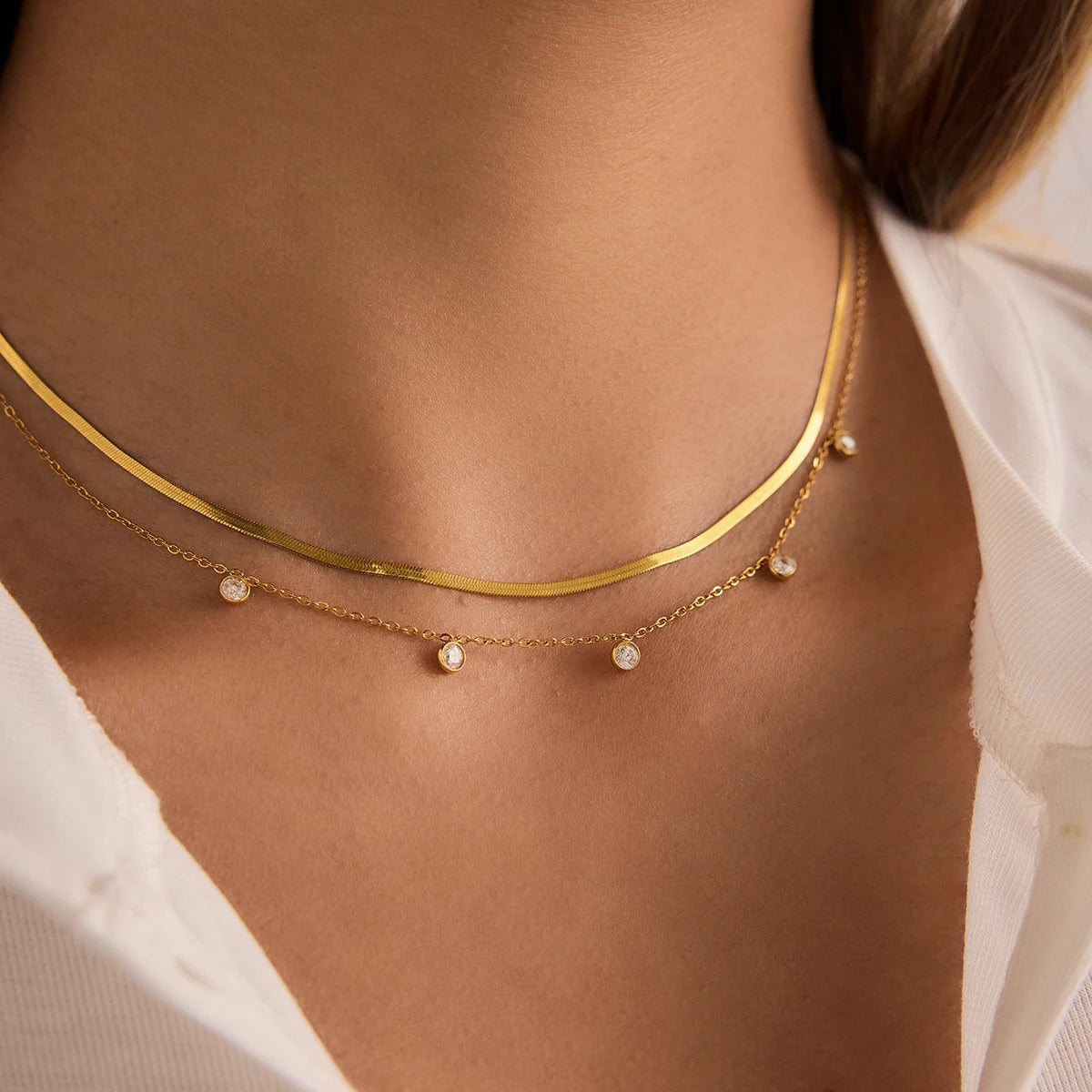 Detailansicht eines geschichteten Halskettensets aus goldvergoldetem Edelstahl am Hals einer Trägerin, das das modern-elegante Paperclip-Design über einem schlichten weißen T-Shirt und einem beige Blazer hervorhebt.