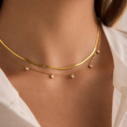 Detailansicht eines geschichteten Halskettensets aus goldvergoldetem Edelstahl am Hals einer Trägerin, das das modern-elegante Paperclip-Design über einem schlichten weißen T-Shirt und einem beige Blazer hervorhebt.