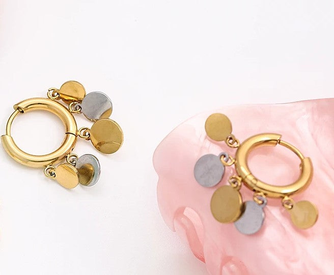 Detailaufnahme der goldenen Plättchen-Ohrringe platziert auf einer glänzenden, rosafarbenen Schmuckschale.