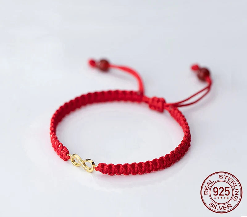Nahaufnahme eines geflochtenen roten Textilarmbands mit vergoldetem Unendlichkeitszeichen aus 925er Sterling Silber auf neutralem Hintergrund.