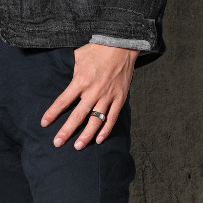 Ein Mann mit der Hand an der Jeans-Tasche trägt den breiten, silbernen Edelstahl-Designring lässig am Ringfinger.