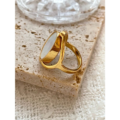Nahaufnahme eines goldfarbenen Rings mit schimmernder Perlmutt-Einlage auf einer strukturierten Oberfläche, 18 Karat vergoldet.