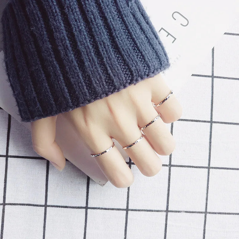 Minimalistischer Ear- und Finger-Schoking-Look: Mehrere zarte facettierte Ringe an einer Hand auf kariertem Untergrund