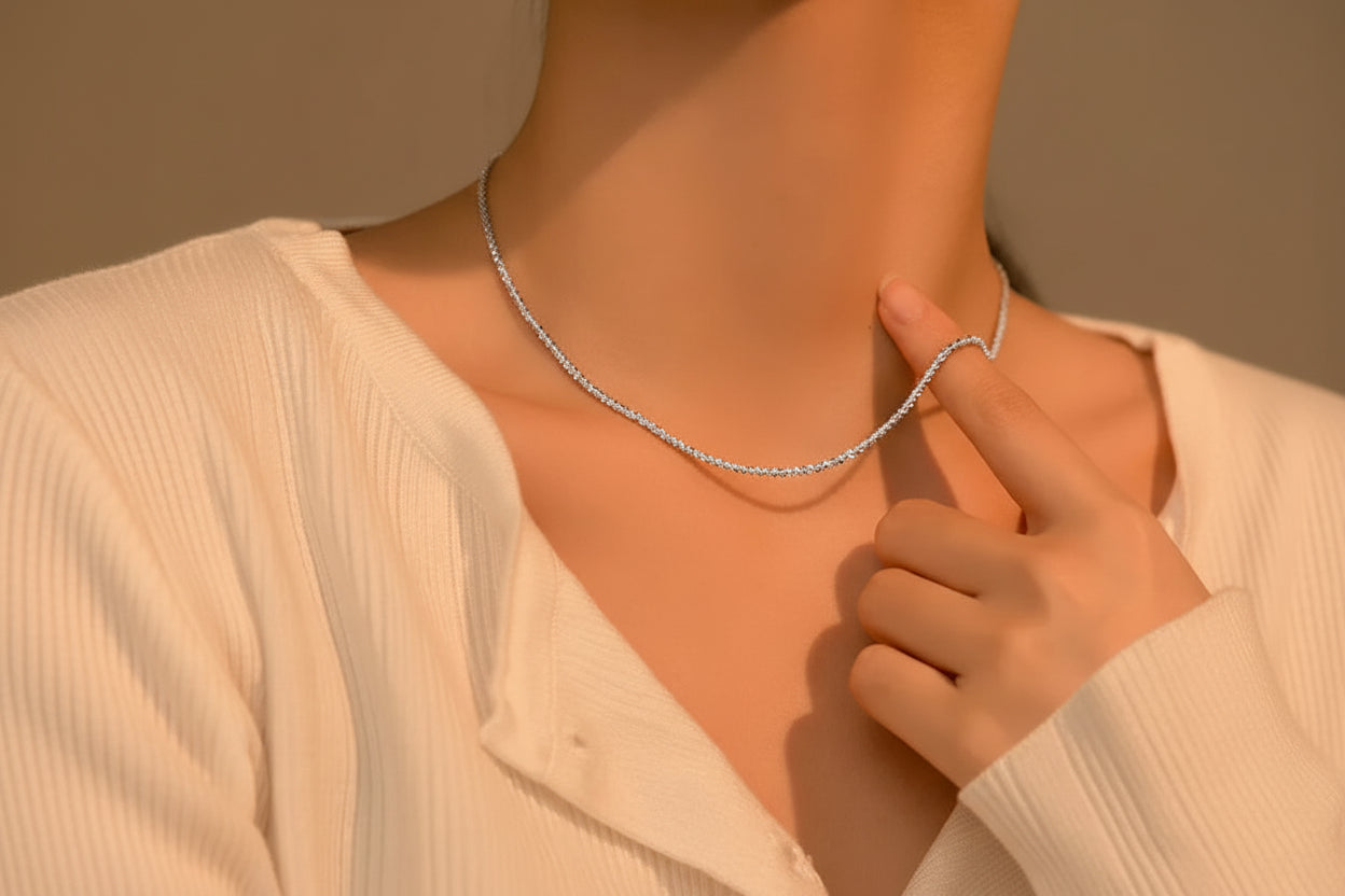 „Minimalistisches Tragebild einer zierlichen Kugelkette aus 925er Silber am Hals einer Frau, kombiniert mit einer weißen, gerippten Strickjacke.“