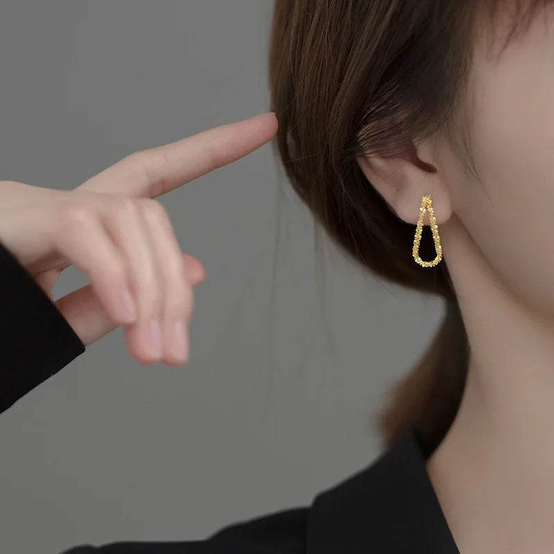 Seitenansicht einer Frau, die einen kleinen, tropfenförmigen (oder U-förmigen) goldfarbenen Ohrring (vermutlich vergoldetes 925er Silber) trägt; eine Hand berührt das Ohr.