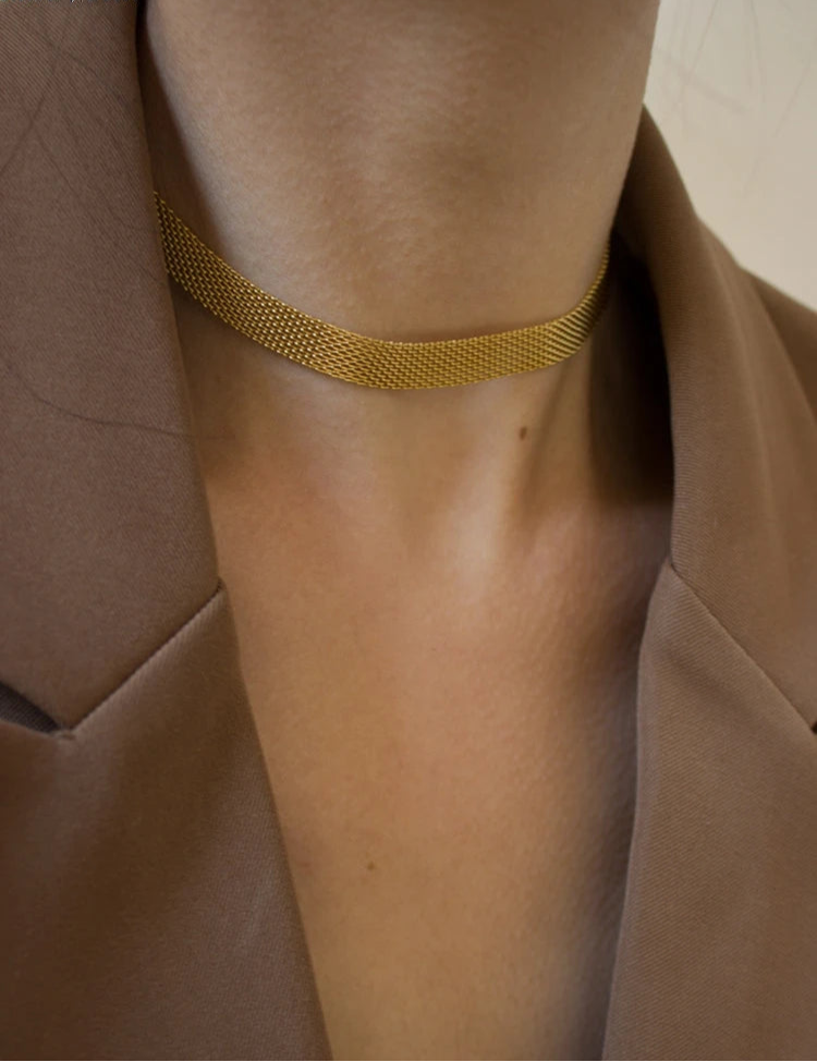Goldene, flache Schlangenkette an Frau getragen | Schimmernder, kurzer Halsschmuck zum Blazer | Gold-Kette elegant