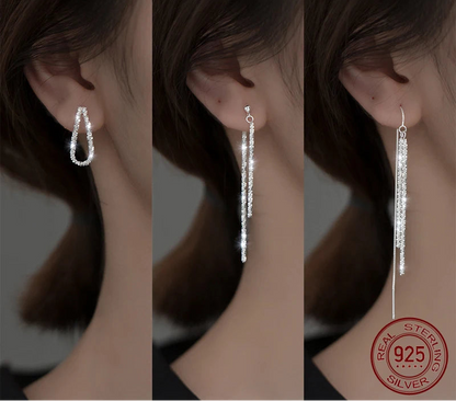  Collage mit drei Ansichten von silberfarbenen Ohrringen aus 925er Silber am Ohr: (Links) Ein mittelgroßer, offener, tropfenförmiger oder U-förmiger Ohrring mit Glitzersteinen. (Mitte) Ein kurzer, doppelsträngiger Faden-Ohrring mit Glitzersteinen. (Rechts) Ein langer, doppelsträngiger Faden-Ohrring mit Stab-Elementen und Glitzersteinen, mit sichtbarem 925er Sterling Silver Echtheitssiegel.