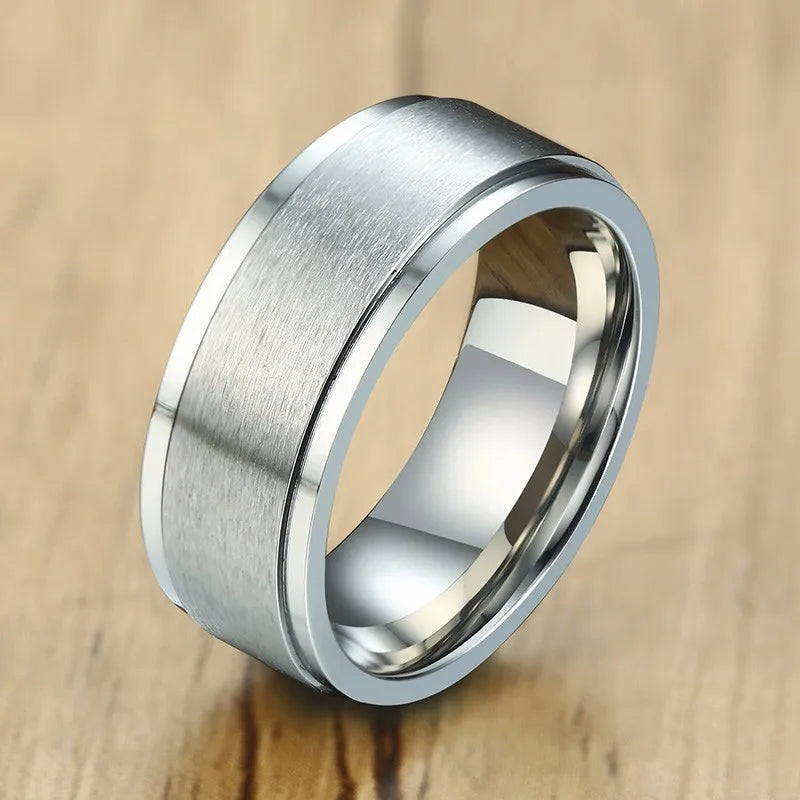 Nahaufnahme eines silberfarbenen Edelstahl-Spinner-Rings mit gebürstetem äußeren Ring und glänzend poliertem inneren Ring, liegend auf einer glatten Oberfläche.