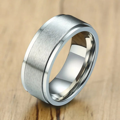 Nahaufnahme eines silberfarbenen Edelstahl-Spinner-Rings mit gebürstetem äußeren Ring und glänzend poliertem inneren Ring, liegend auf einer glatten Oberfläche.