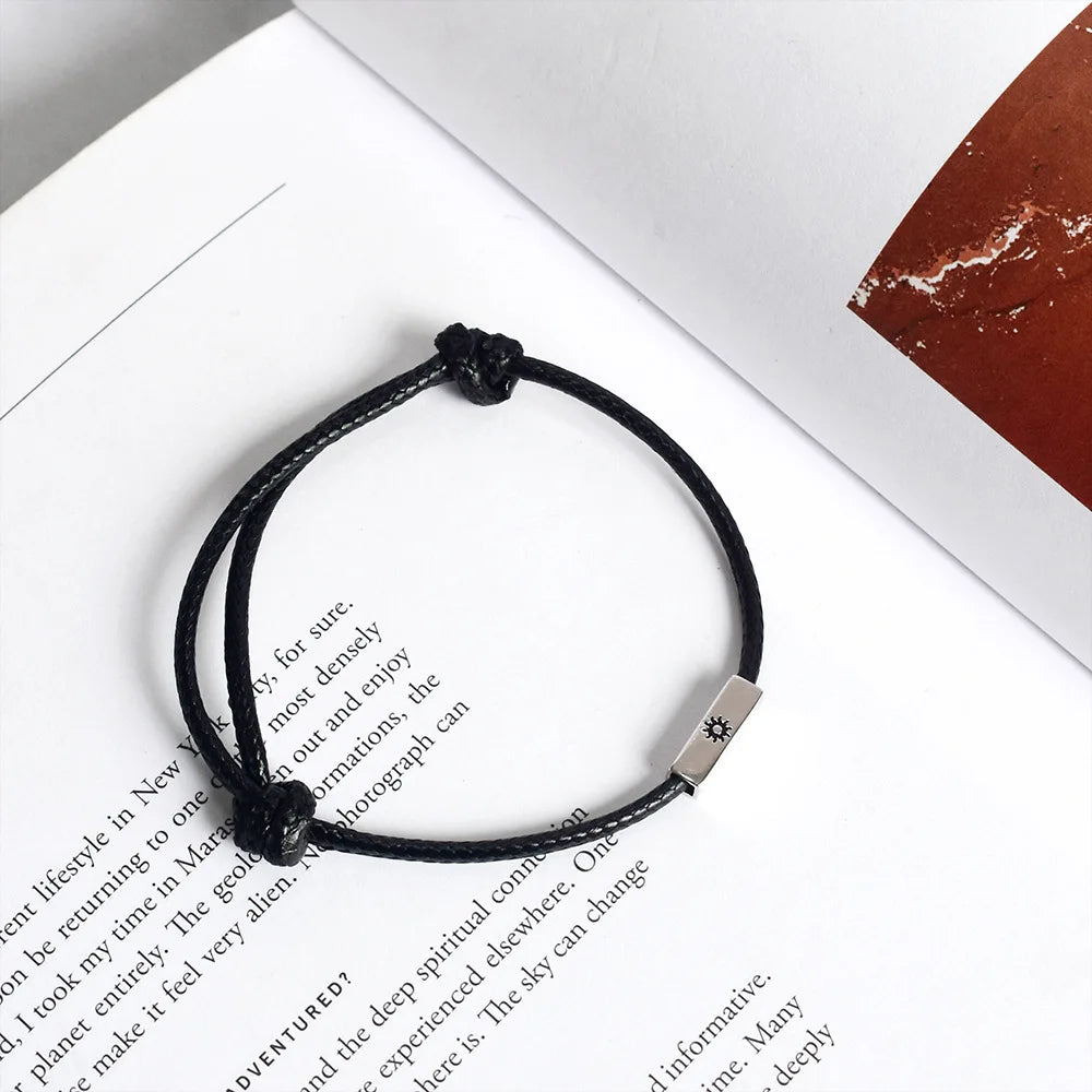 Produktfotografie des schwarzen Kordelarmbands mit Sonne-Gravur elegant auf einem geöffneten Buch platziert.