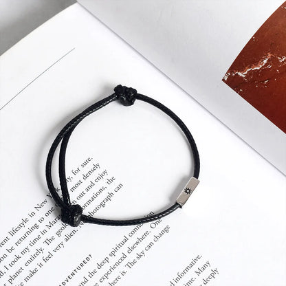 Produktfotografie des schwarzen Kordelarmbands mit Sonne-Gravur elegant auf einem geöffneten Buch platziert.