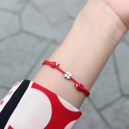 Filigranes rotes Textilarmband mit 925er Silber-Kleeblatt am Handgelenk einer Frau getragen.