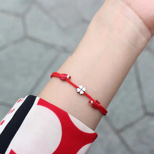 Filigranes rotes Textilarmband mit 925er Silber-Kleeblatt am Handgelenk einer Frau getragen.