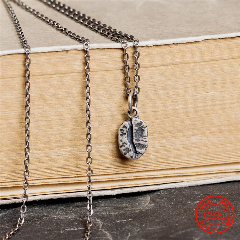 Nahaufnahme einer detailreichen Kaffeebohnen-Kette aus geschwärztem 925er Sterling Silber im Vintage-Stil, hängend an einem alten Buch.