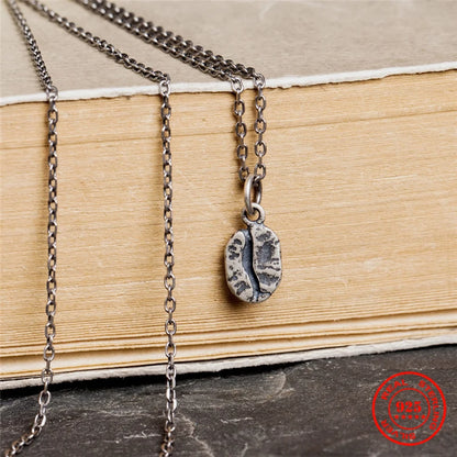 Nahaufnahme einer detailreichen Kaffeebohnen-Kette aus geschwärztem 925er Sterling Silber im Vintage-Stil, hängend an einem alten Buch.