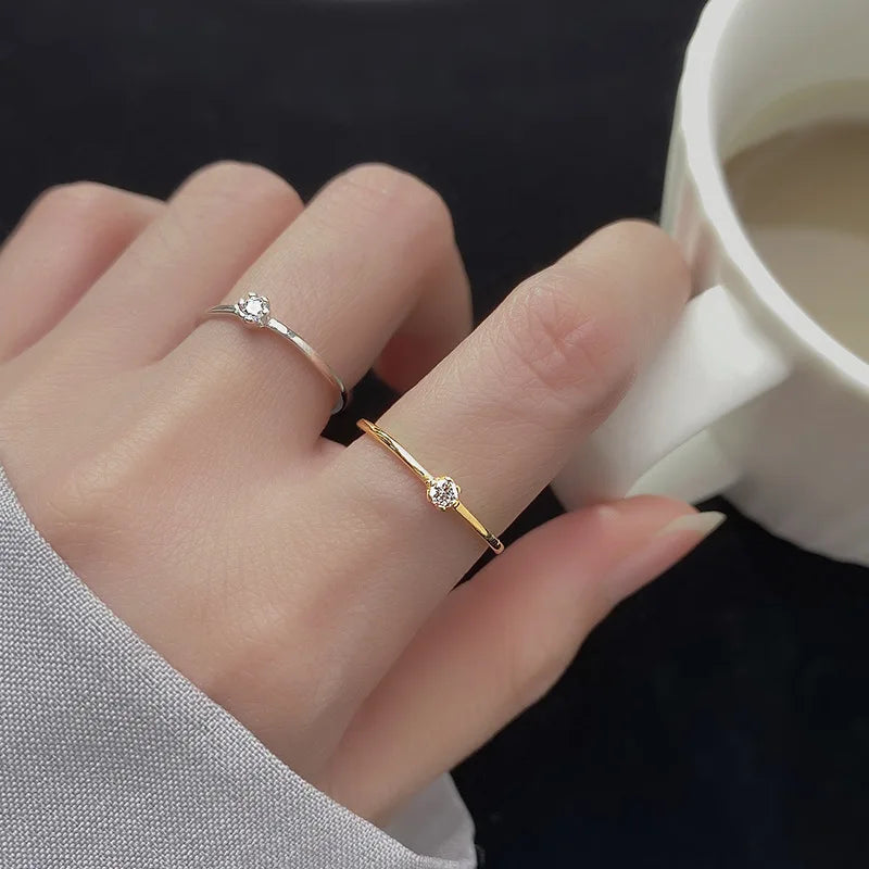 Minimalistische Trageansicht: Kombinierte zarte Solitärringe aus Silber und Gold an der Hand mit einer Tasse