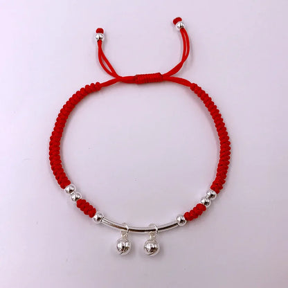 Draufsicht des verstellbaren roten Kordelarmbands mit silbernen Glöckchen und Zugverschluss auf weißem Hintergrund.