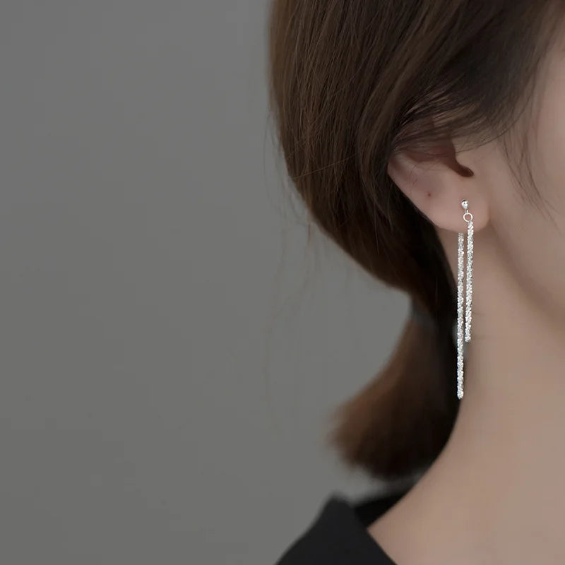 Seitenansicht einer Frau, die ein Paar mittellange, doppelsträngige Faden-Ohrringe aus silberfarbenem 925er Silber trägt.