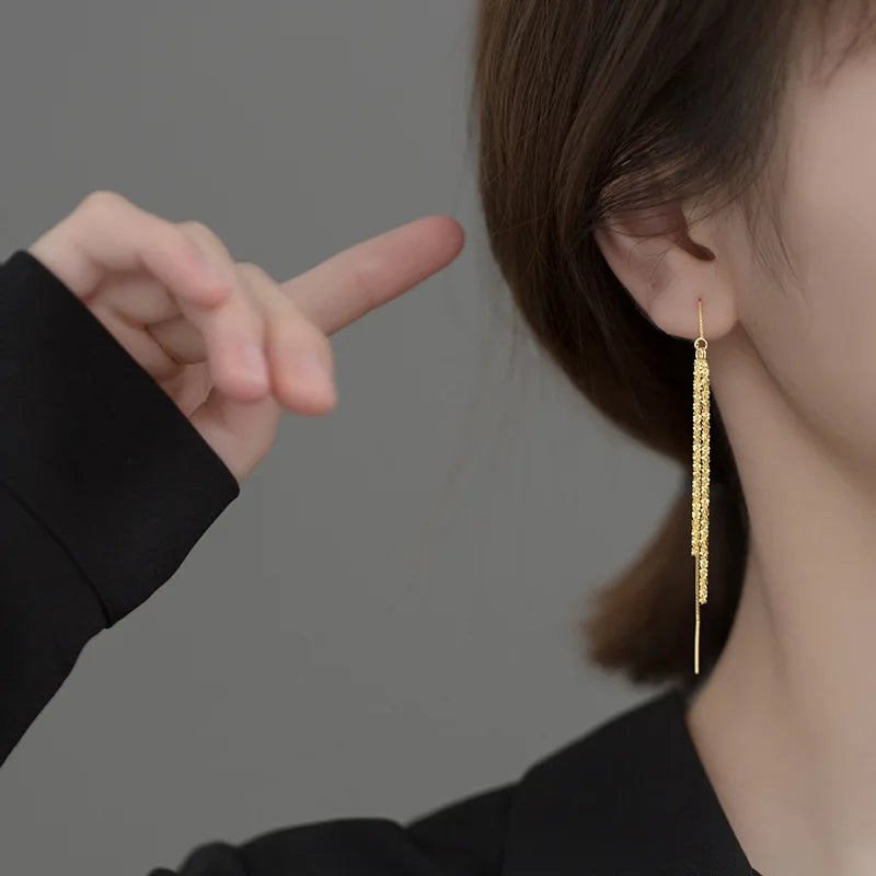 Seitenansicht einer Frau, die einen extra langen, goldfarbenen Faden-Ohrring aus 925er Silber (vergoldet) trägt; eine Hand berührt leicht das Haar.