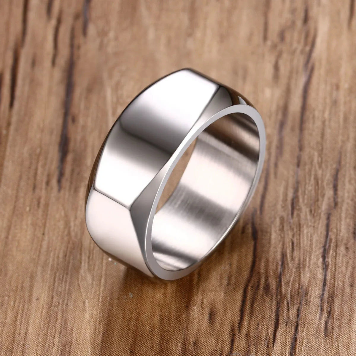Nahaufnahme eines geometrischen Herrenrings aus hochglanzpoliertem Edelstahl mit abgeflachter Oberseite, präsentiert auf einer Holzoberfläche.