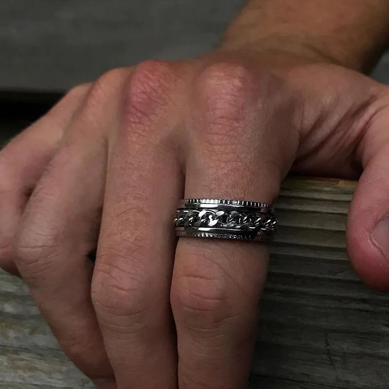Nahaufnahme einer Männerhand, die einen breiten Edelstahl-Spinner-Ring mit einem beweglichen Panzerketten-Mittelelement am Zeigefinger trägt.