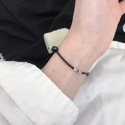 Schwarz gekleidete Person trägt das verstellbare Kordelarmband mit silbernem Motiv-Element am Handgelenk.